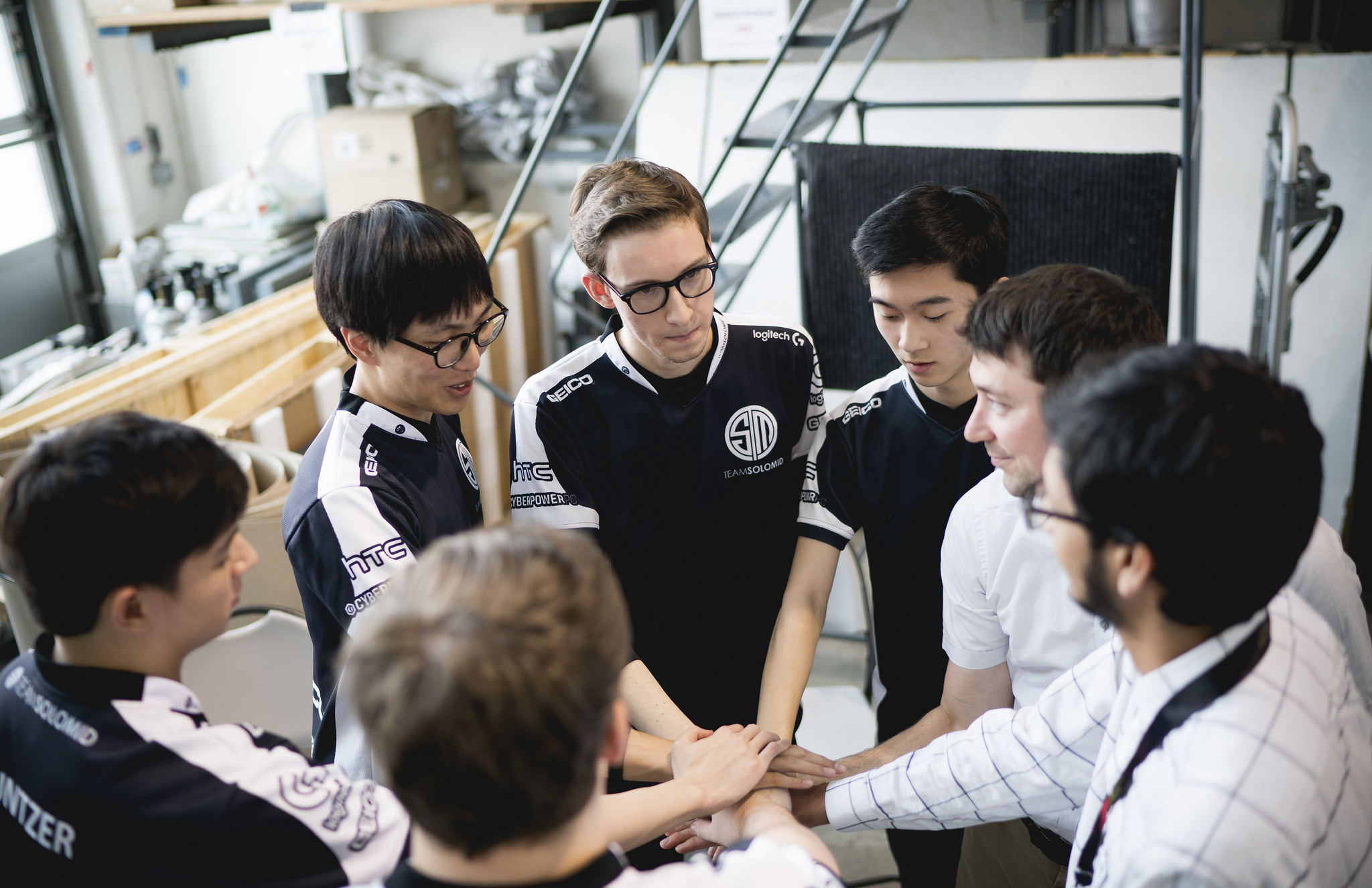 A photo of Team SoloMid (TSM) standing in a circle and putting their hands together in the middle.